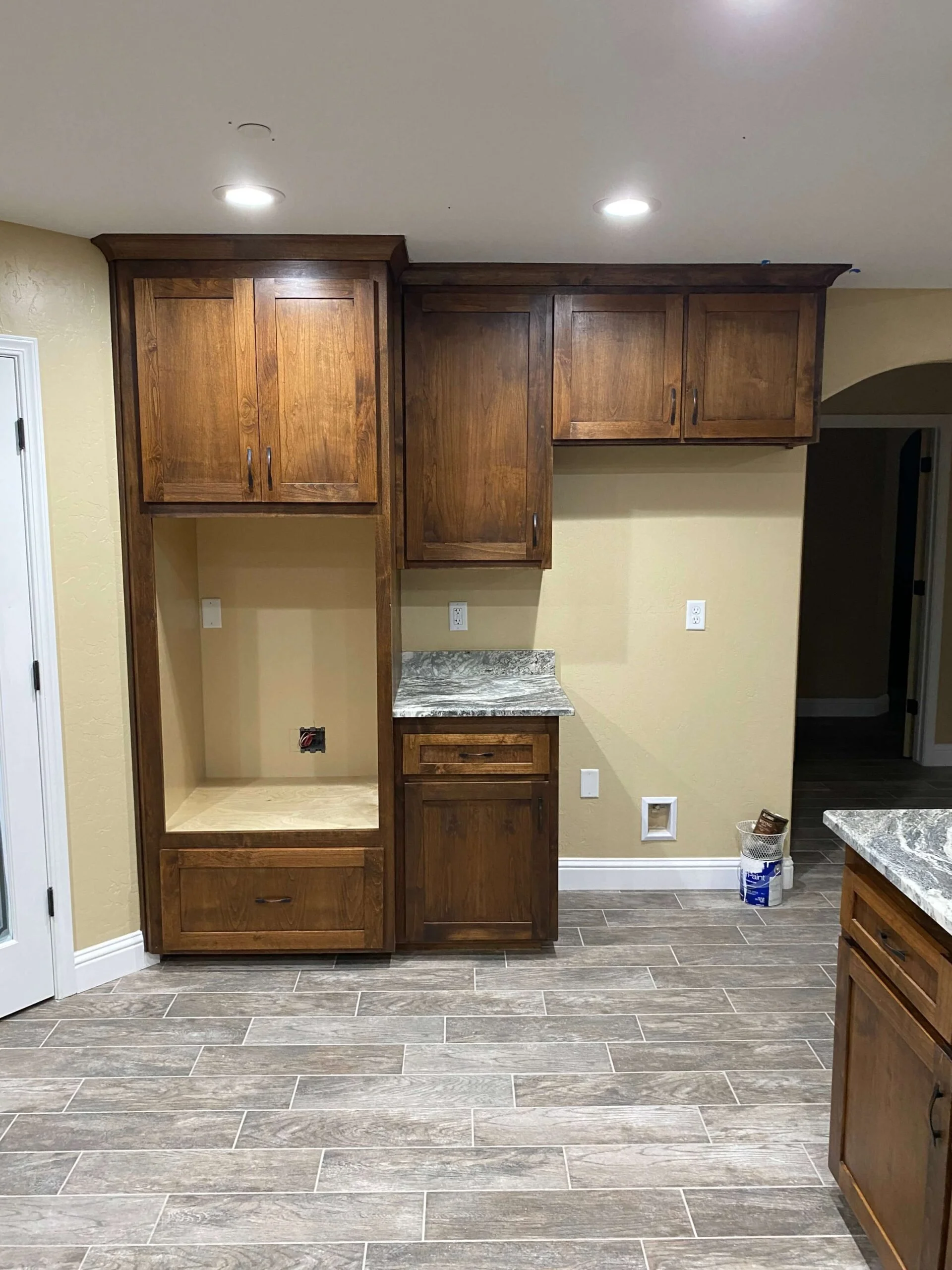 Kitchen cabinetry with wooden upper and lower cabinets, a countertop with a marble pattern, and some construction or renovation materials on the floor.