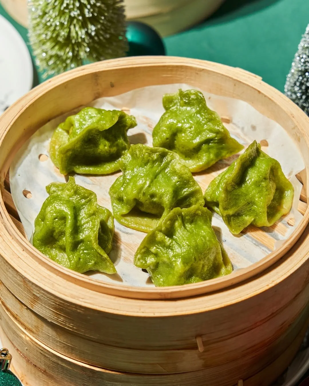 Green steamed dumplings in a bamboo steamer basket.