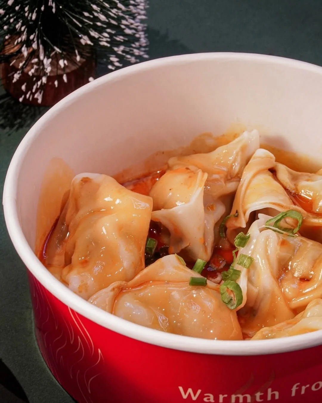 Close-up of a red and white container filled with steamed dumplings garnished with chopped green onions.