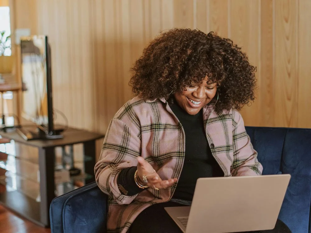 African American woman sitting on a couch working on a laptop.