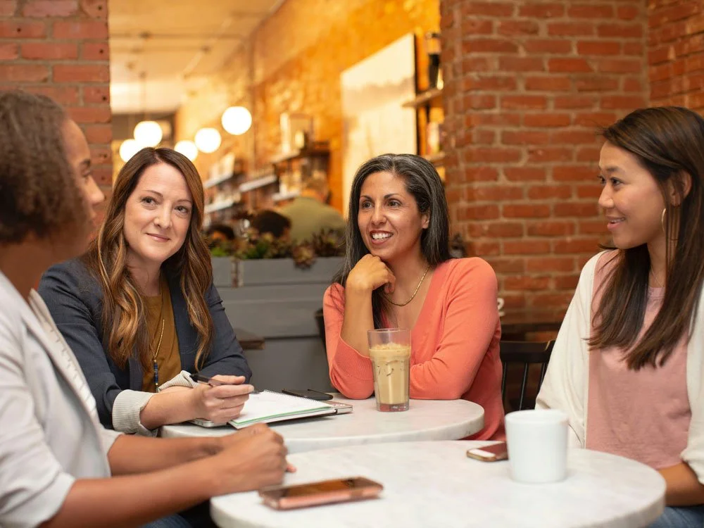Group of four diverse women sitting at a table in a coffee shop.