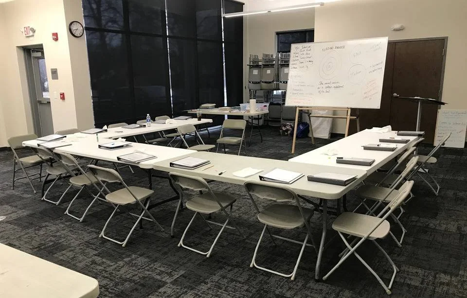 Conference room with U-shaped table arrangement, chairs, notebooks, pens, and whiteboard from The ACT Mom's in-person class.