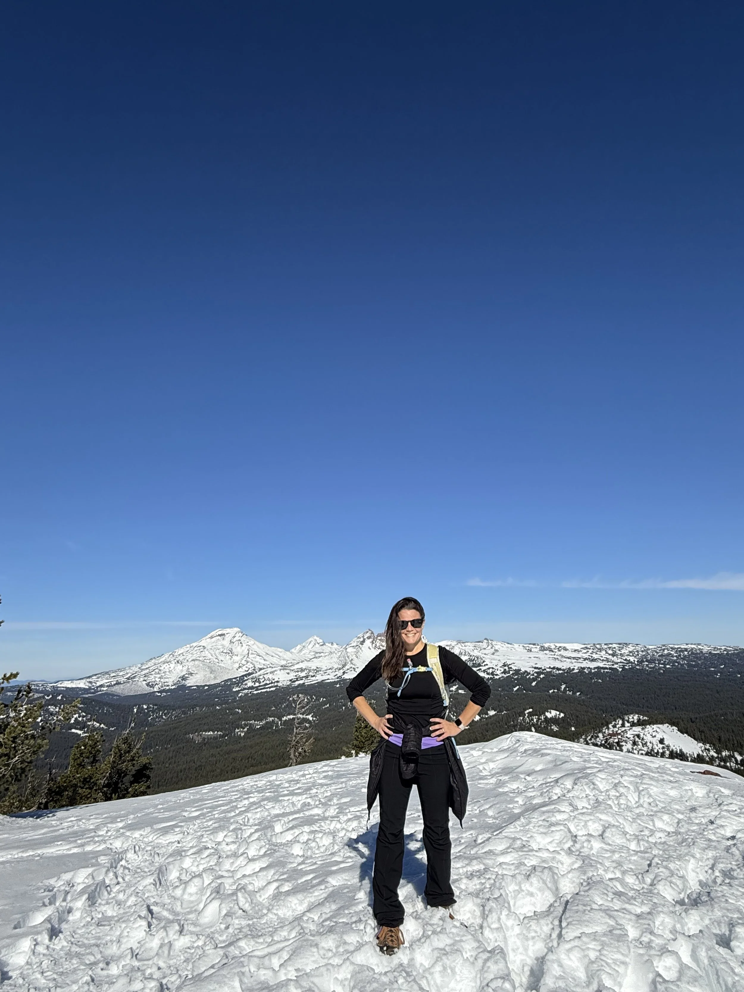 Angie Watson at the top of Tumalo Mountain with the Three Sisters Mountains in the background in Bend, Oregon.