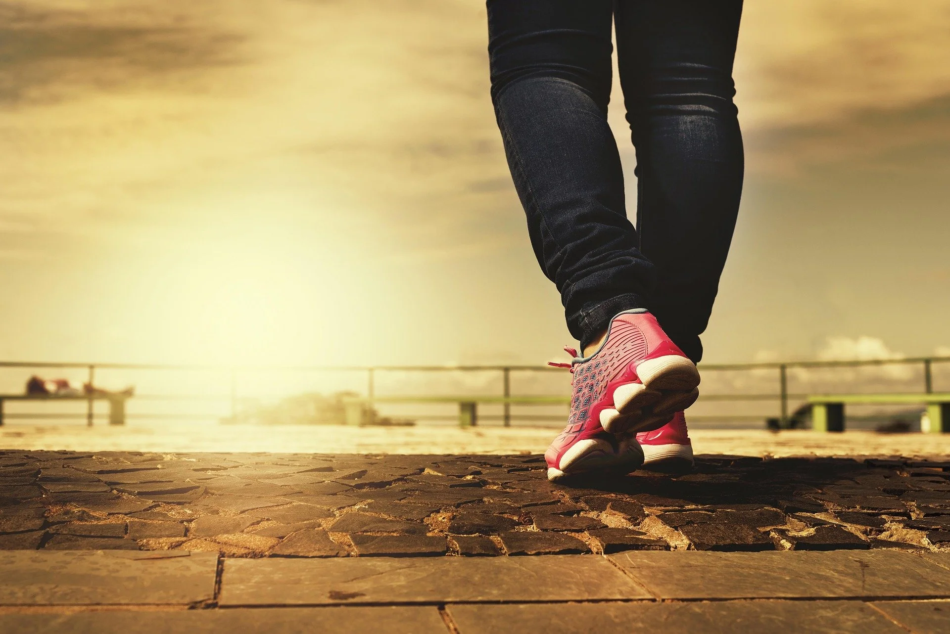 woman's legs walking on pier toward sun