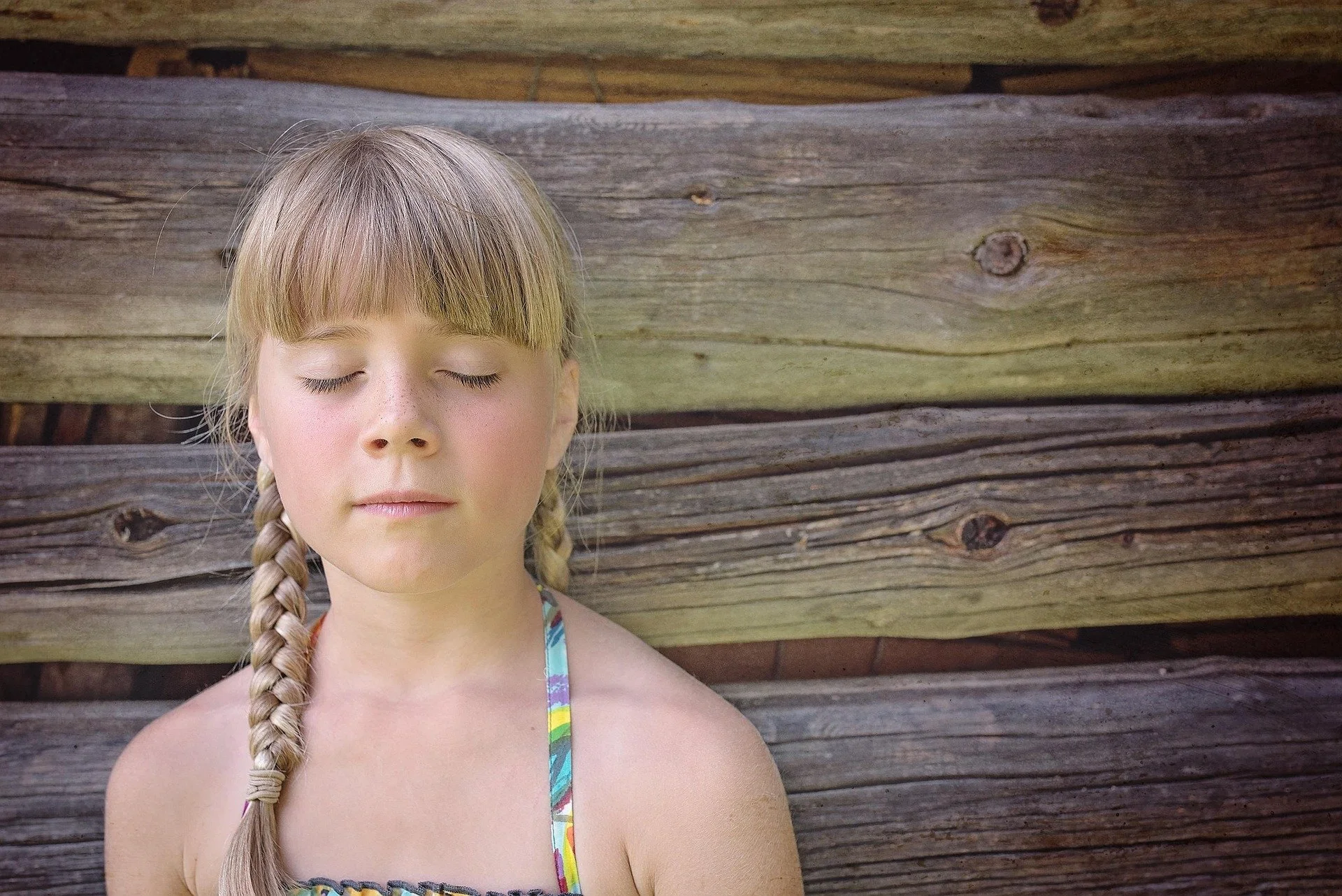 blond girl, eyes closed, in front of wooden wall