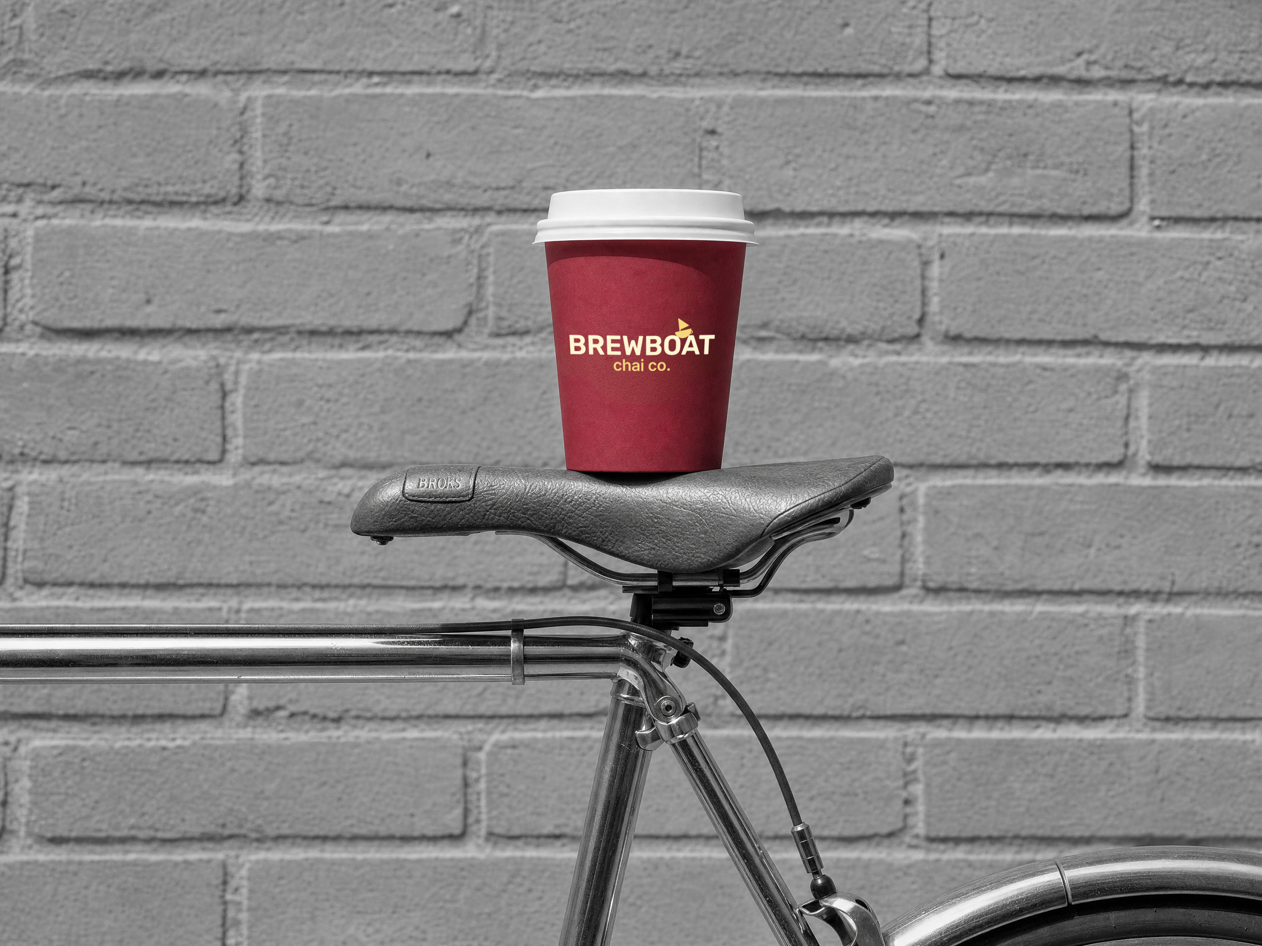 Brewboat chai cup resting on a bicycle against a grey brick wall.
