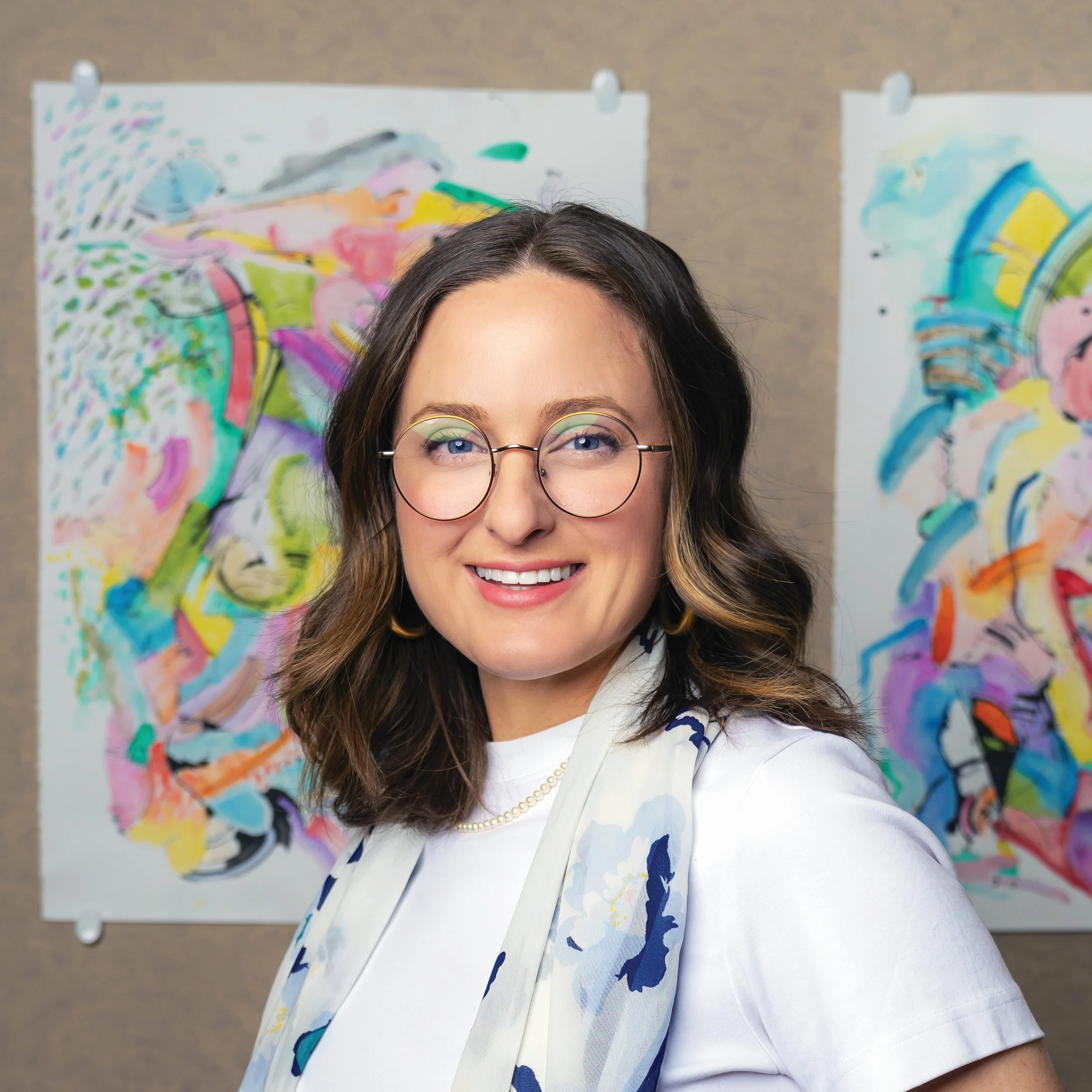 Aly Maier Lokuta, the Assistant Vice President at the Arts & Well-Being, New Jersey Performing Arts Center, smiling, with colorful abstract paintings in the background.