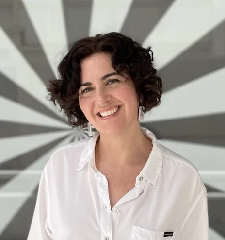 Danielle Acerra, the Artist and Managing Director of the National Organization for Arts in Health (NOAH), smiling in front of a black-and-white radial background.