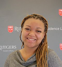 Kendra Lewis, the Research Coordinator at the Center for Health, Identity, Behavior and Prevention Studies (CHIBPS), Rutgers School of Public Health, smiling in front of a grey Rutgers University background.