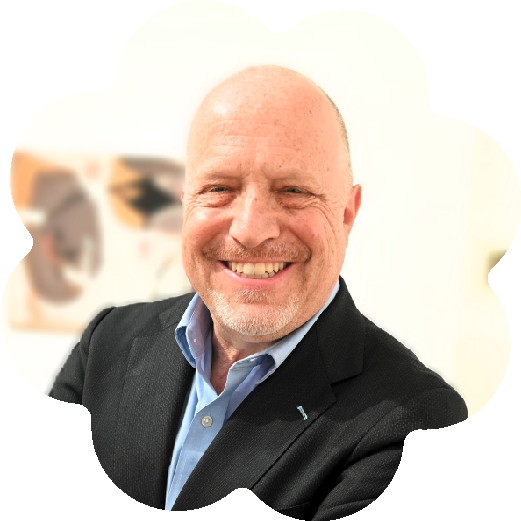 Randy Cohen, Vice President of Research at Americans for the Arts (AFTA), wearing a black blazer and light blue shirt, standing inside a room with blurry artwork in the background.