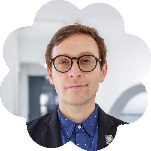 Marcel W. Foster, the CEO & Co-Founder of Performance Hypothesis and DPhil Researcher at Oxford University (PRS), wearing a dark blazer, and a blue patterned shirt, standing in a modern indoor setting with white walls and a blurred background.