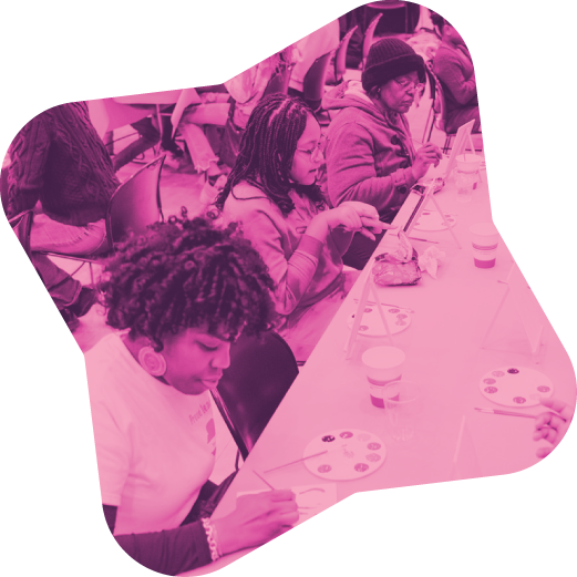 People sitting at a long table painting on canvases in an art class.