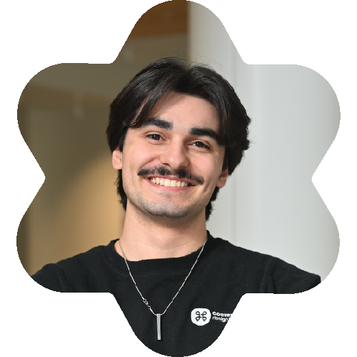 Carlos Mosca, freelance Graphic Designer, wearing a black sweater with a logo and necklace, in an indoor setting.