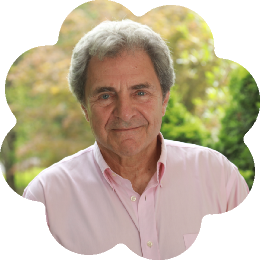 Eric Booth, the International Arts Learning Consultant/Author and Co-founder of International Teaching Artists Collaborative (ITAC), wearing a pink button-up shirt, standing outdoors with blurred foliage in the background.