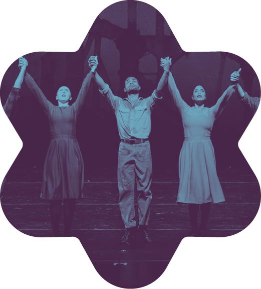 Three actors are standing on stage, holding hands and raising them in celebration, with a theater set in the background.