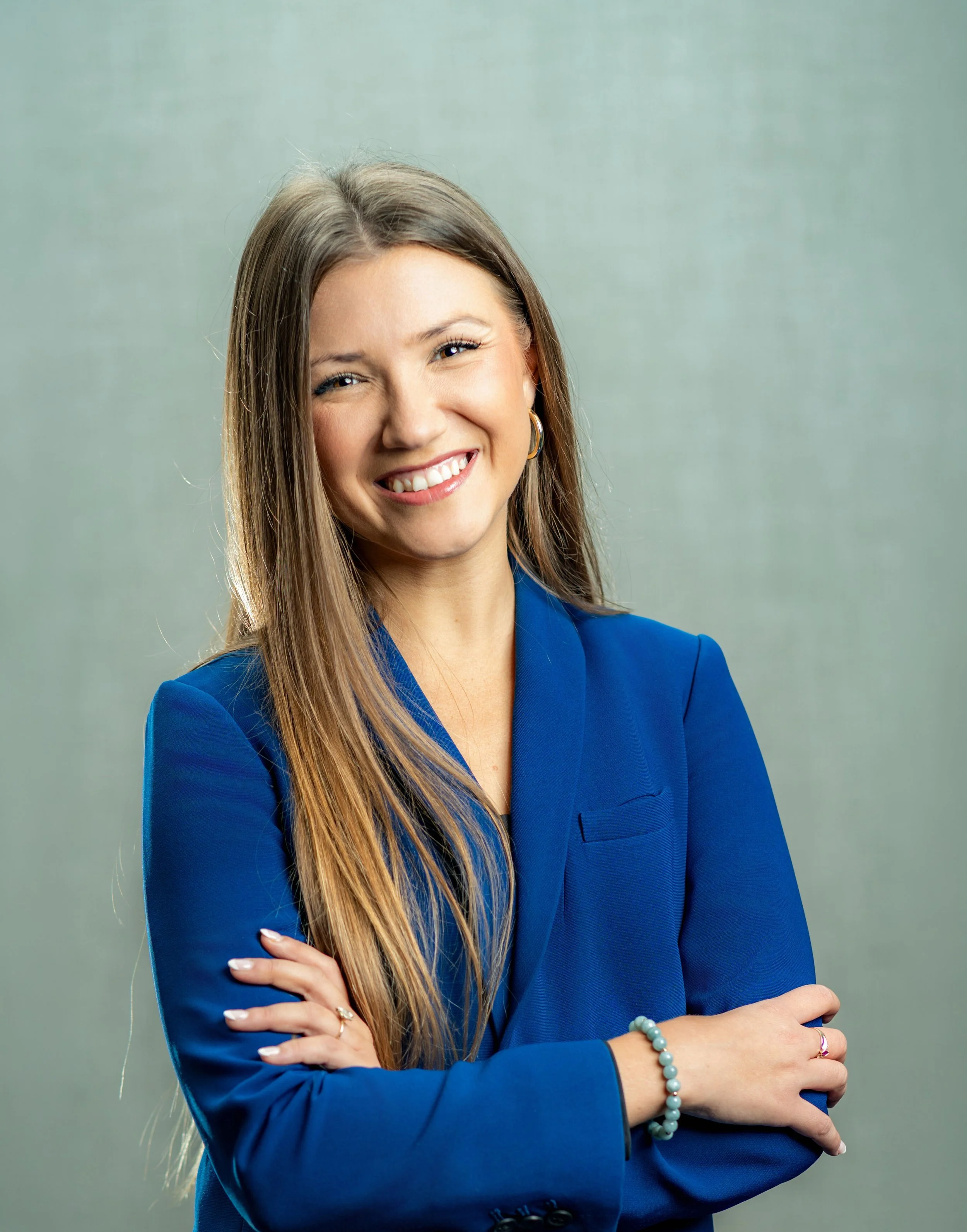 Alexandra K. Rodriguez, Researcher at the Center for Arts in Medicine and Adjunct Faculty at the UF College of Public Health & Health Professions, wearing a blue blazer, standing against a plain pastel green background, with her arms crossed.