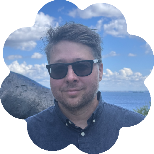 Ryan Stubbs, Chief Program and Strategy Officer at the National Assembly of State Arts Agencies, wearing sunglasses and a dark button-up shirt outdoors, with mountains, ocean, and cloudy sky in the background.