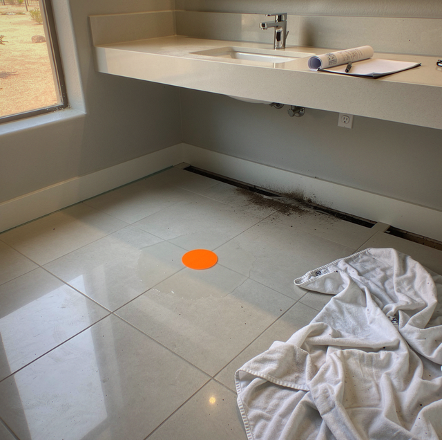A red spill on tile floor beneath a wooden cabinet with a clipboard and papers on top.