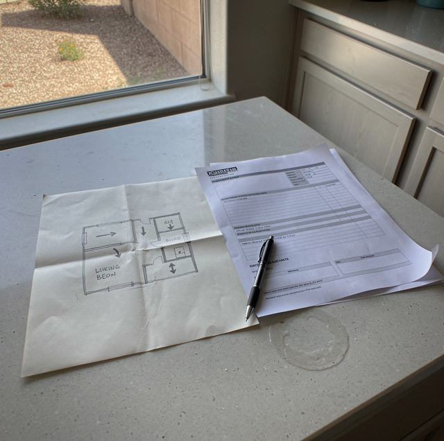 Papers and a pen sit on a windowsill next to a floor plan sketch and printed form.