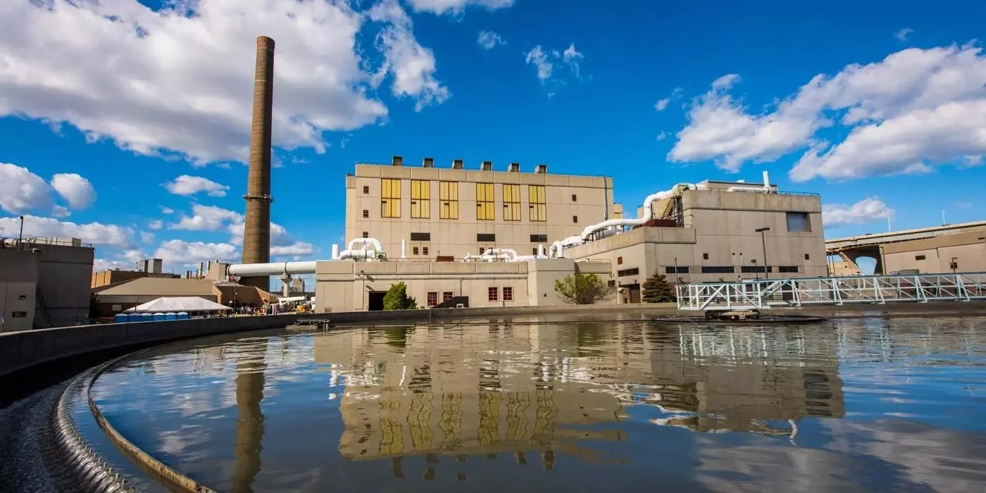 Image of MMSD Veolia Milwaukee Jones Island facility, which serves more than 1 million people across 29 communities , against a partly cloudy blue sky and water below it.