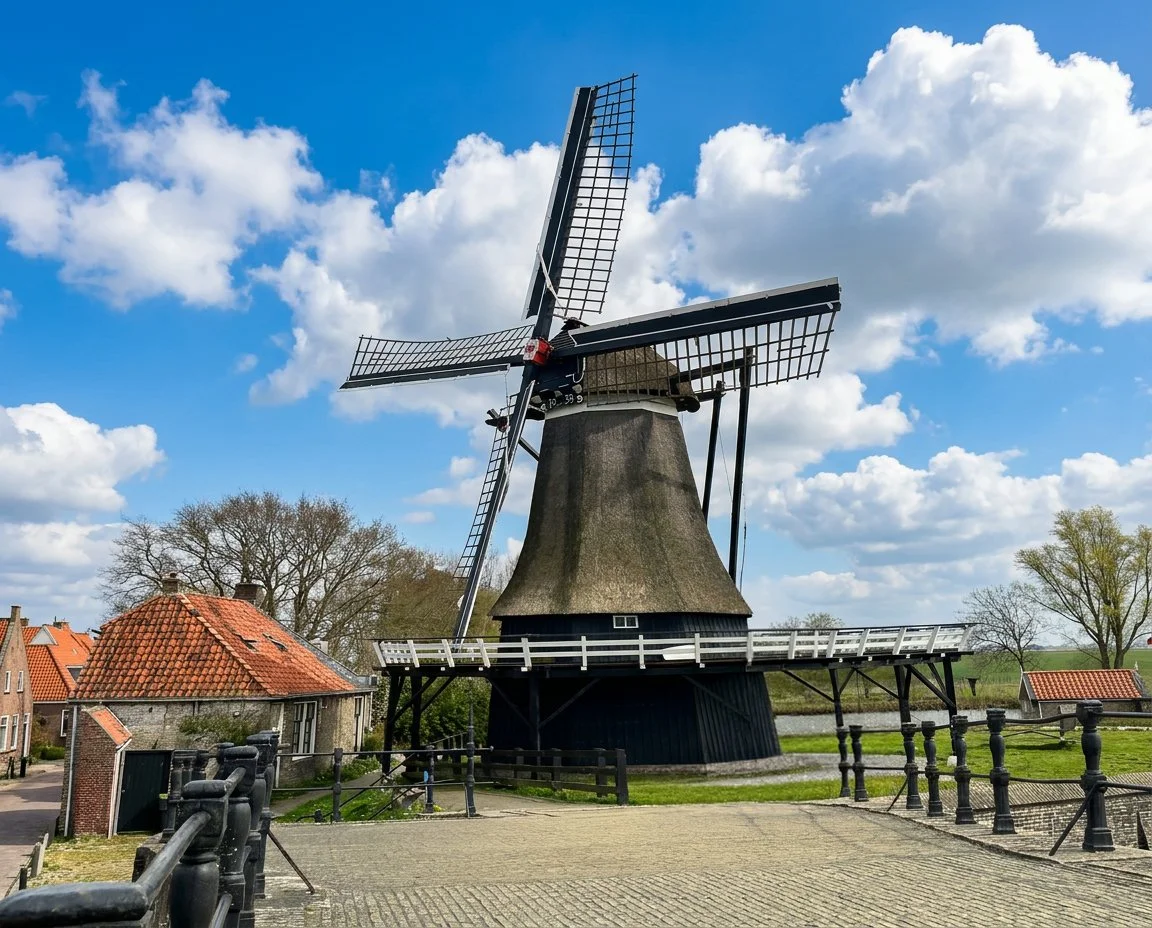 A thatched Dutch windmill beside a canal, with a brick cottage and a white wooden bridge in the foreground