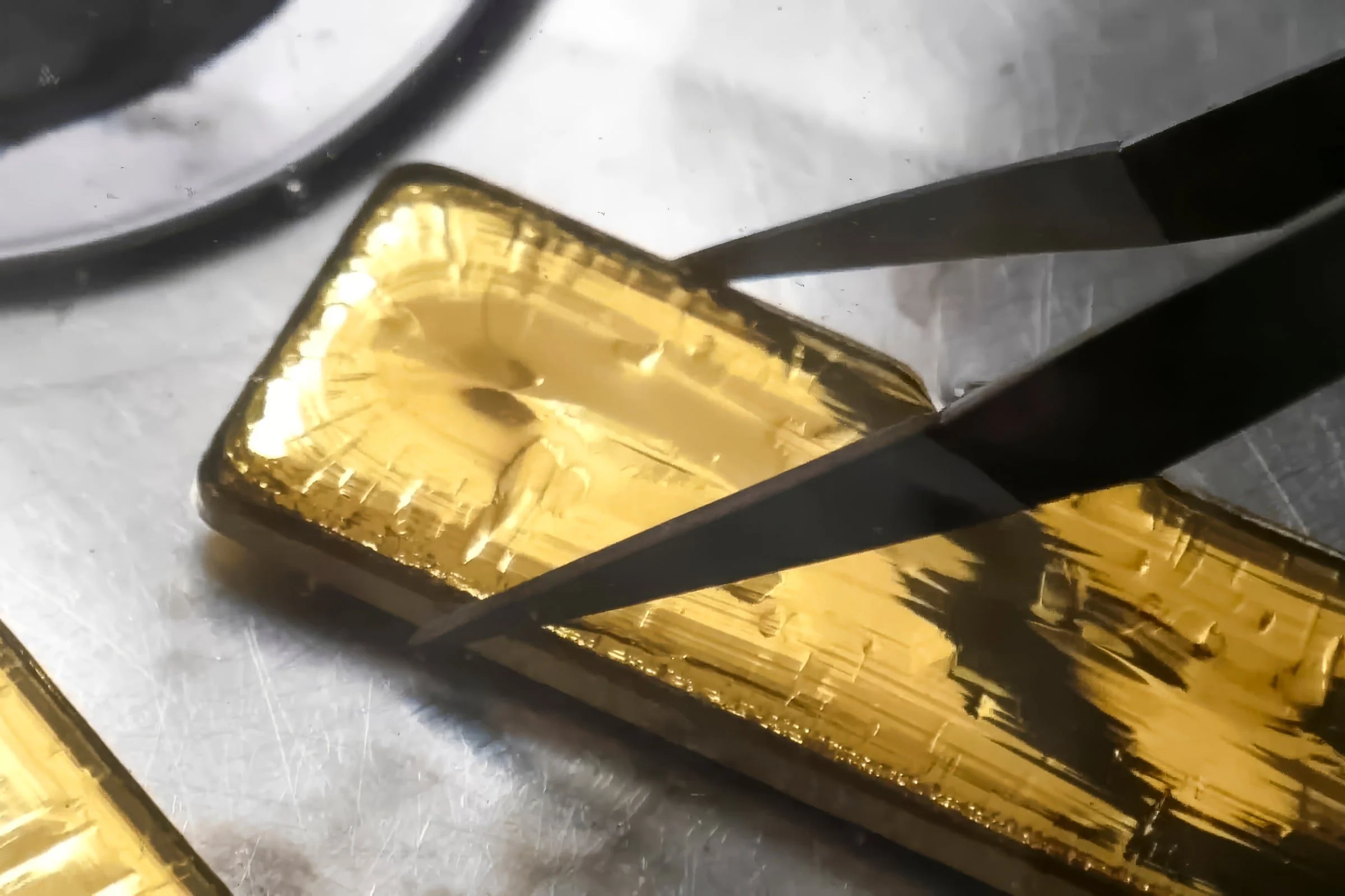 Cast gold bar held with tongs on a metal work surface