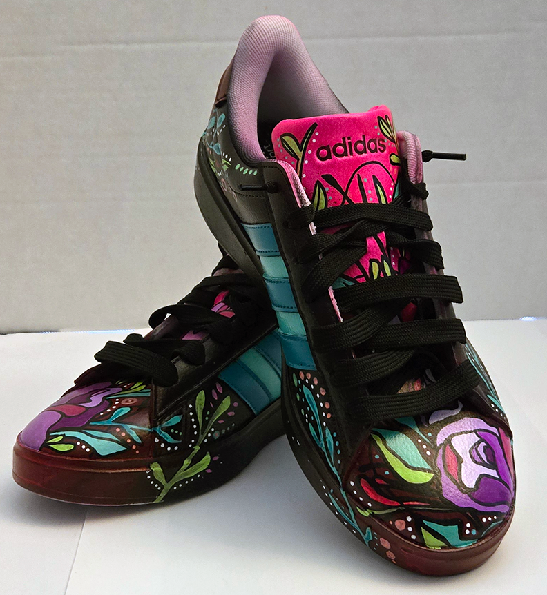Colorful Adidas sneakers with floral and leaf designs painted on black background, featuring pink, purple, blue, green, and white accents, with black laces and a pink tongue.