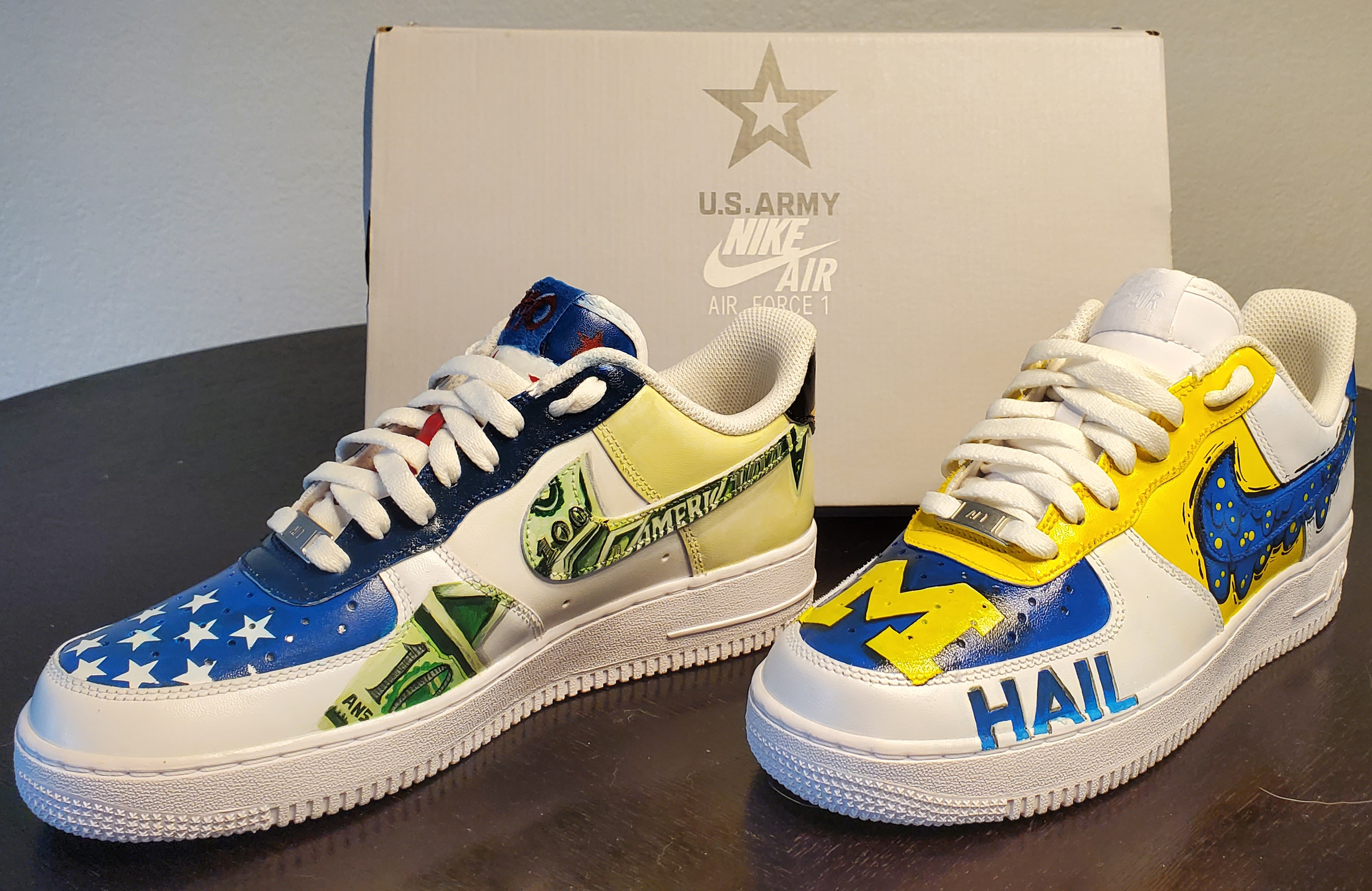 Colorful sneakers featuring American flag stars, dollar bill pattern, and comic-style designs, positioned in front of a white U.S. Army Nike Air Force 1 box.