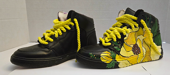 Pair of black high-top sneakers, one shoe decorated with yellow floral patterns, yellow laces, and green leaves.