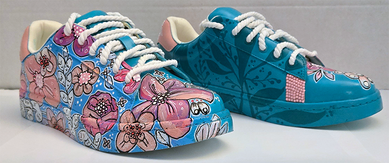 Pair of decorated sneakers with floral and floral designs, pink and blue colors, white laces, and white interior lining.