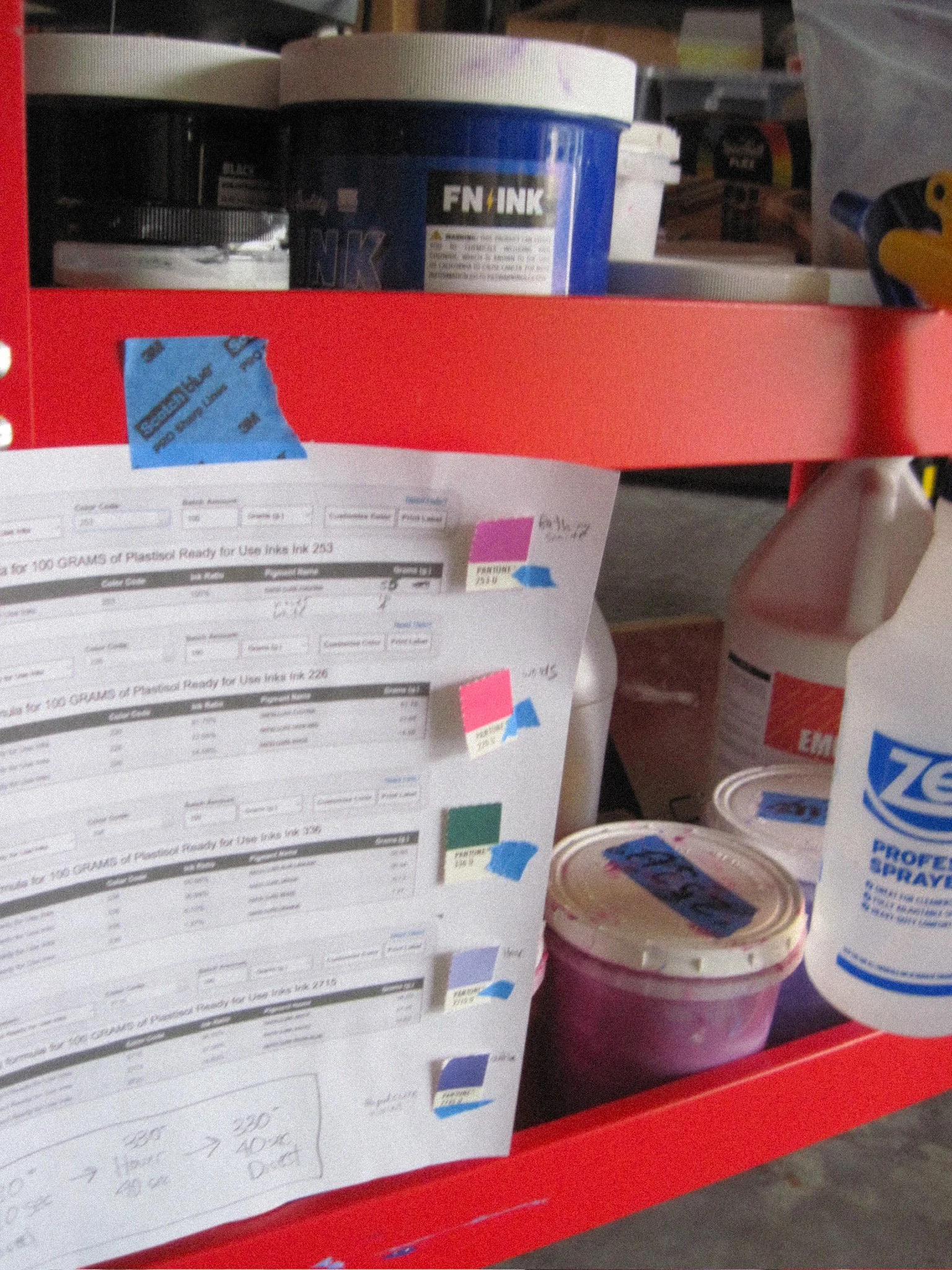 Shelf with various supplies including a container of ink, a roll of tape, a small container of ink, and a container of glue.