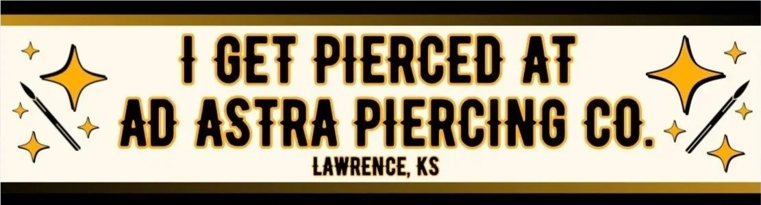 Signboard with humorous text about getting pierced at Astra Piercing Co. in Lawrence, Kansas, decorated with illustrated piercing needles and stars.