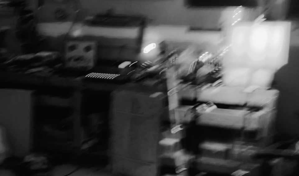 A cluttered room with various appliances, boxes, and furniture, brightly lit by a light source.