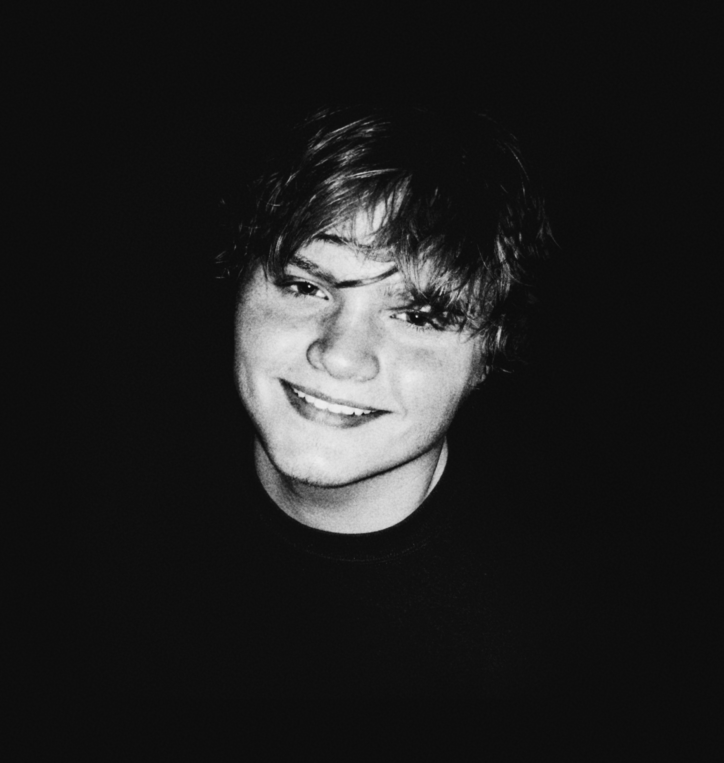 Black and white close-up portrait of a young woman with short, messy hair, smiling slightly with her head tilted to the side.
