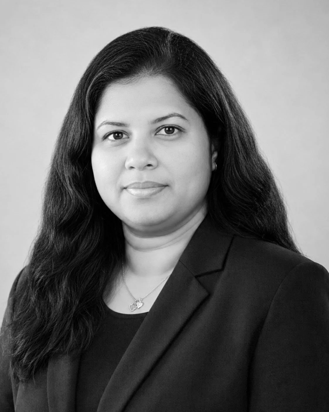 Black and white portrait of a woman with long dark hair wearing a blazer and a necklace.