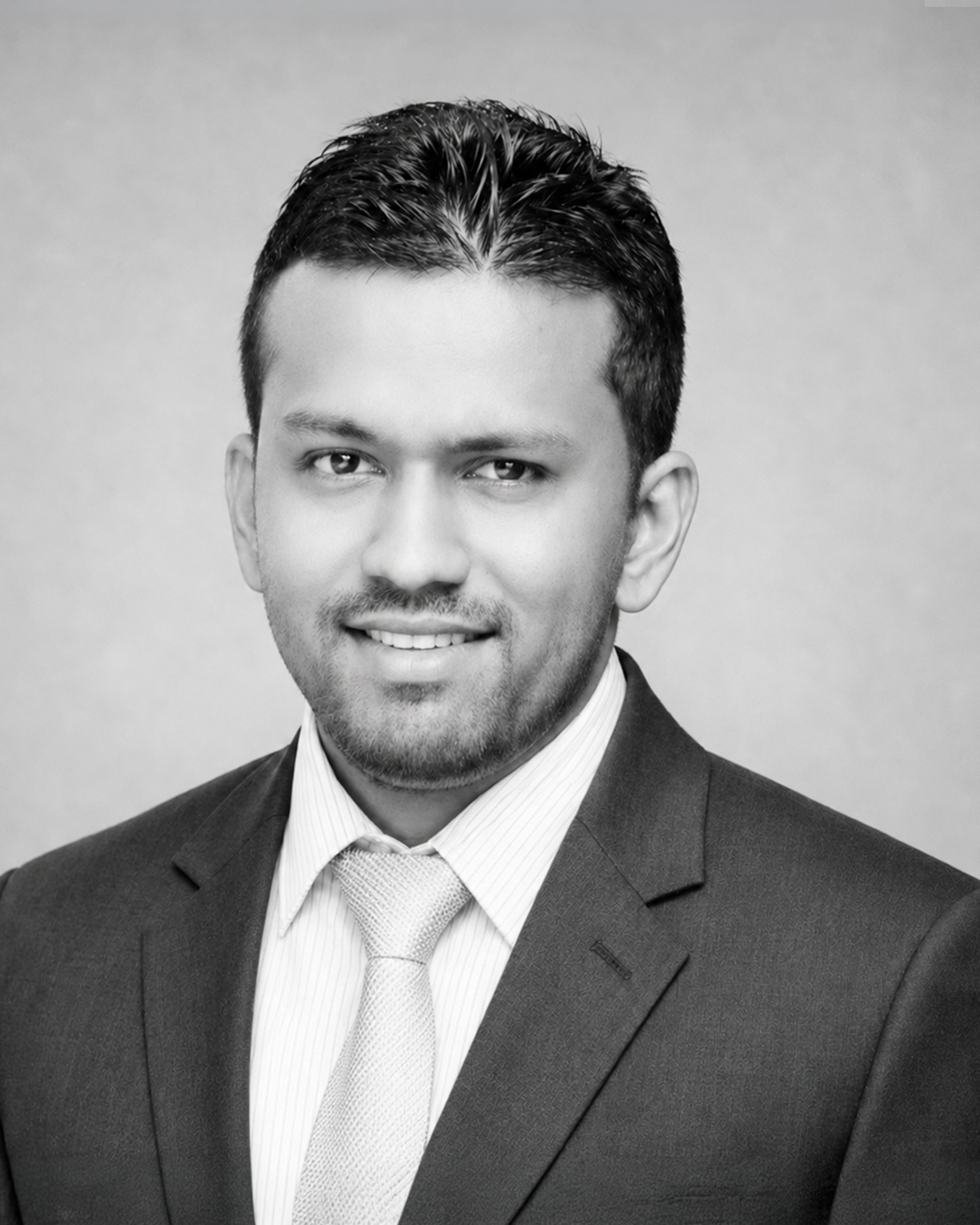 Black and white professional headshot of a man in formal attire, wearing a suit jacket, shirt, and tie, smiling at the camera against a plain background.
