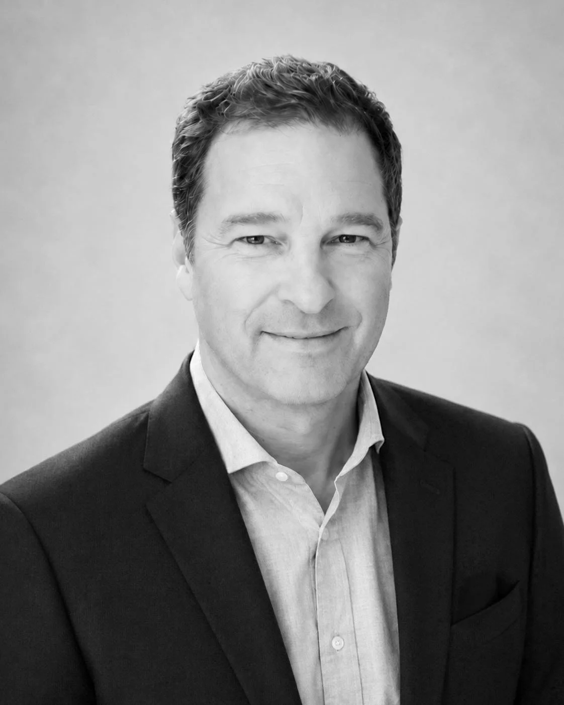 Black and white professional headshot of a man in a suit with a smile, against a plain background.