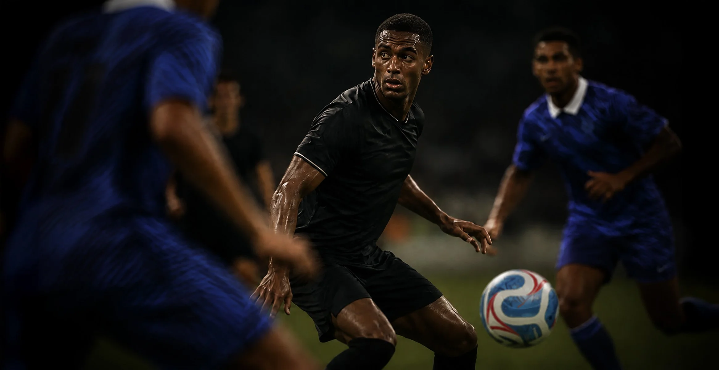 Soccer players in action during a game, with one player in black focusing on the ball while two players in blue are nearby.