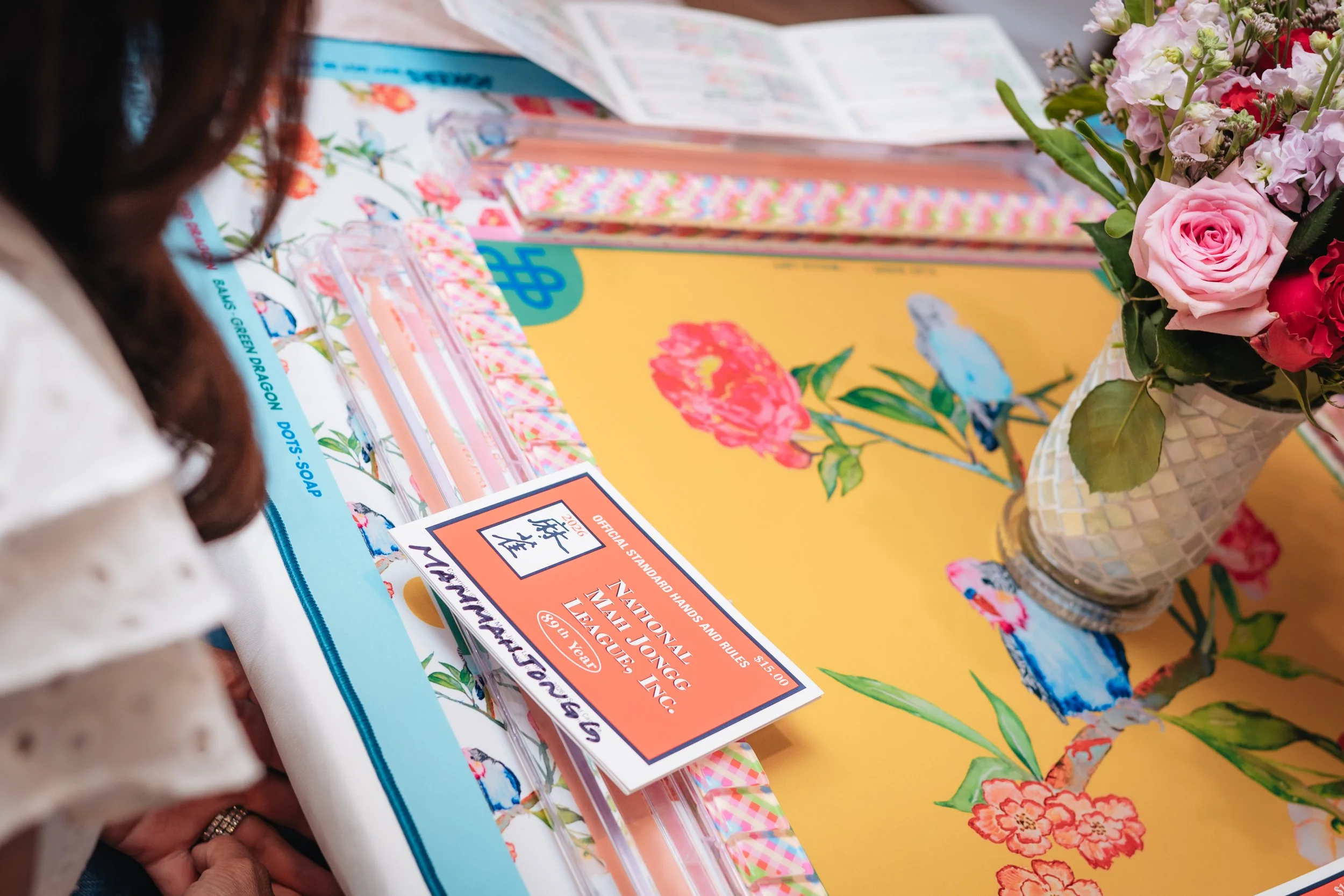 A table covered with colorful promotional materials, a bouquet of pink and red flowers in a decorative vase, and a person with brown hair partially visible on the left side of the image.