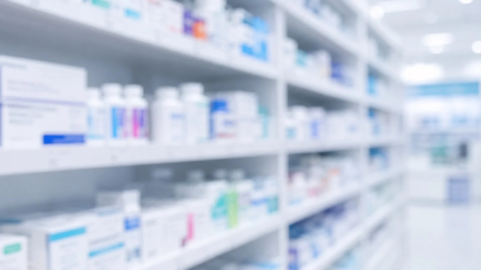Blurred view of pharmacy shelves stocked with bottles and boxes of medications.