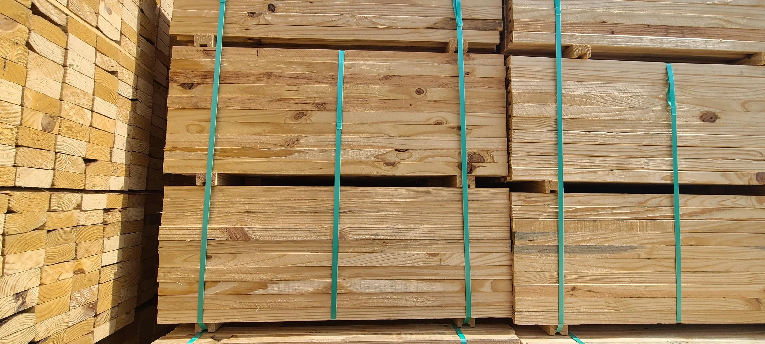 Stacks of lumber wood secured with green straps in a warehouse or store.
