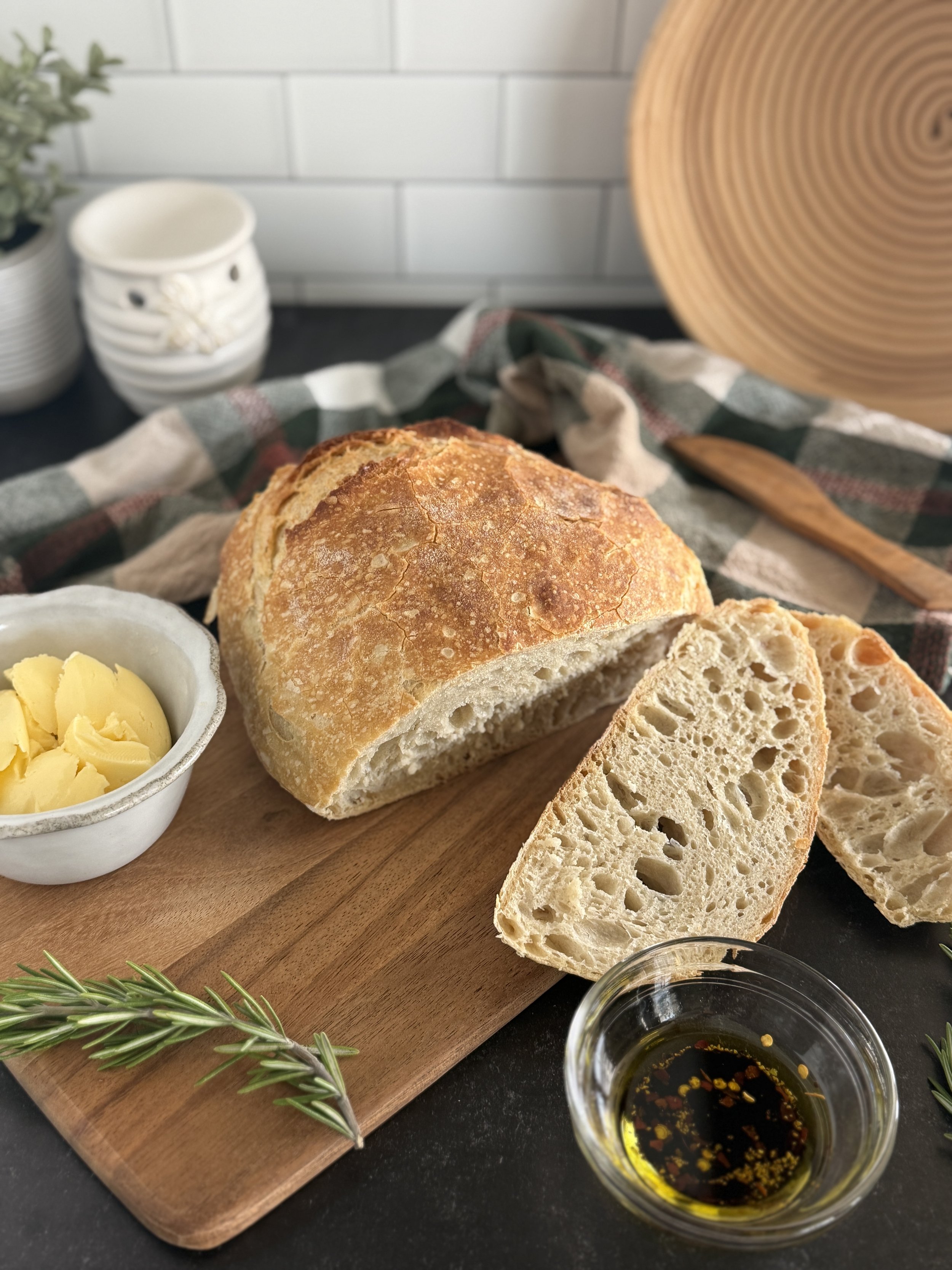 Crusty bread with two slices sliced from it with butter in a white dish beside it.