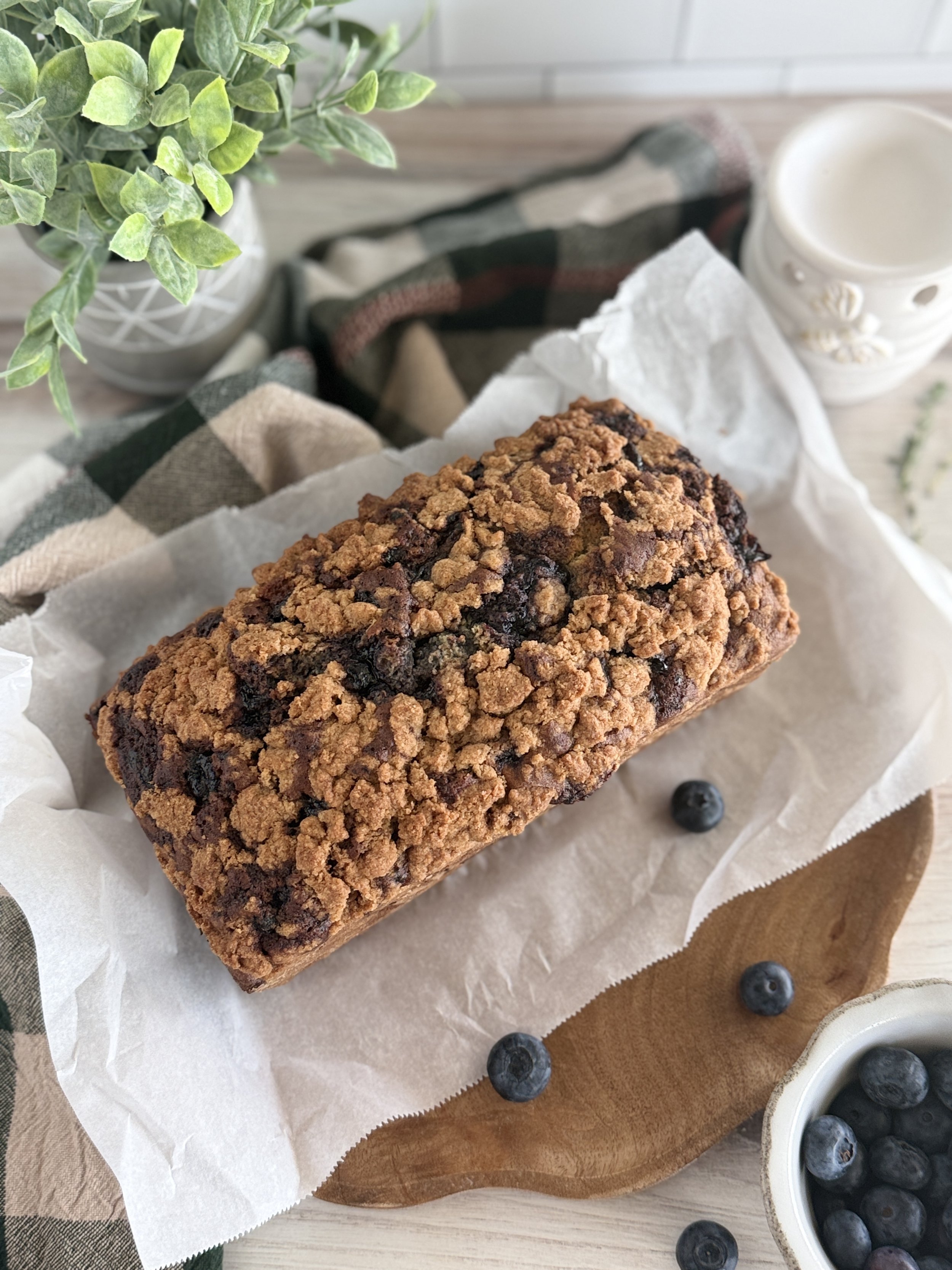 Blueberry bread with crumble on top on a white sheet of parchment paper.