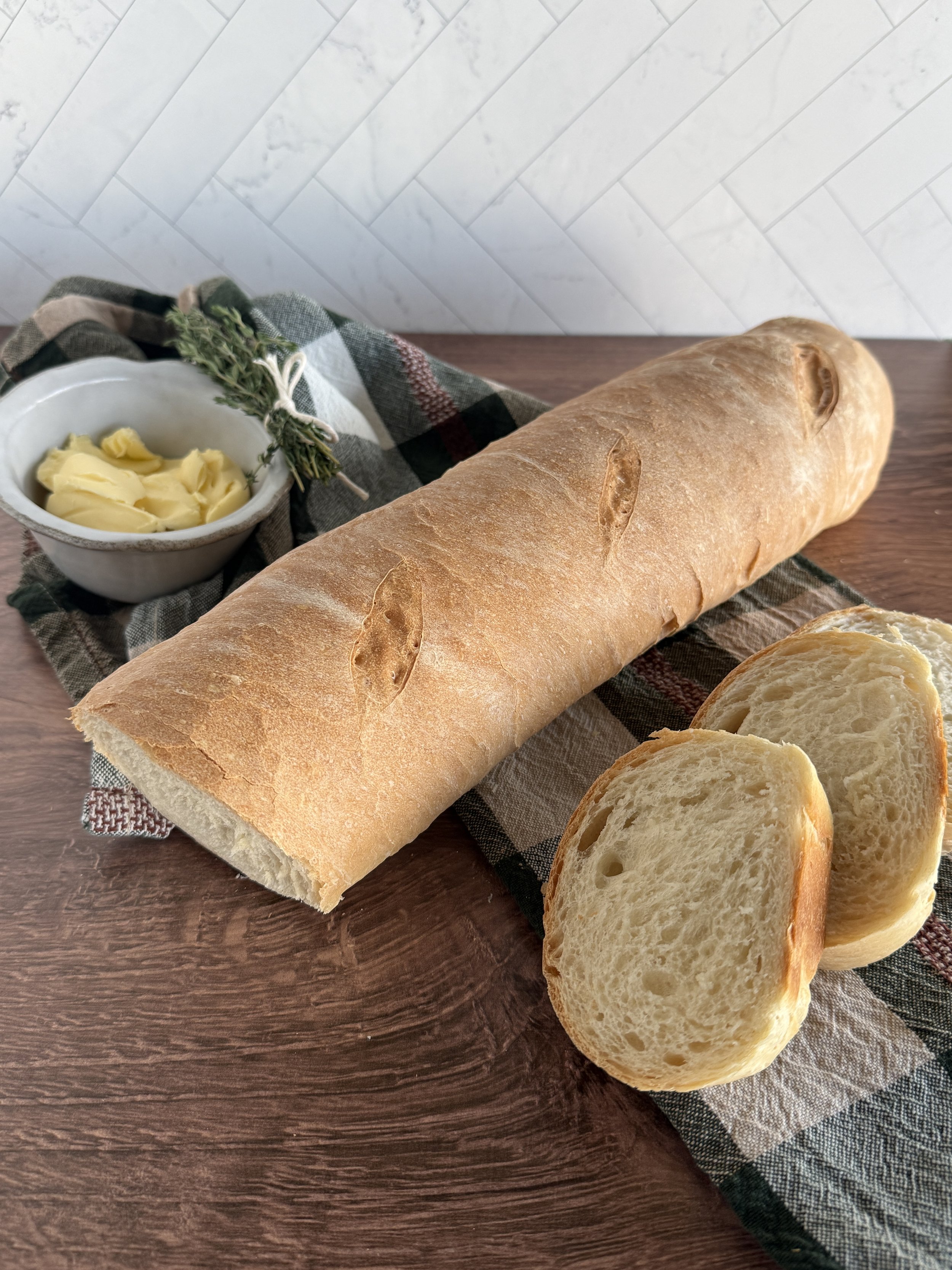 French bread with three slices cut off from it laying on a checkered green and white towel.