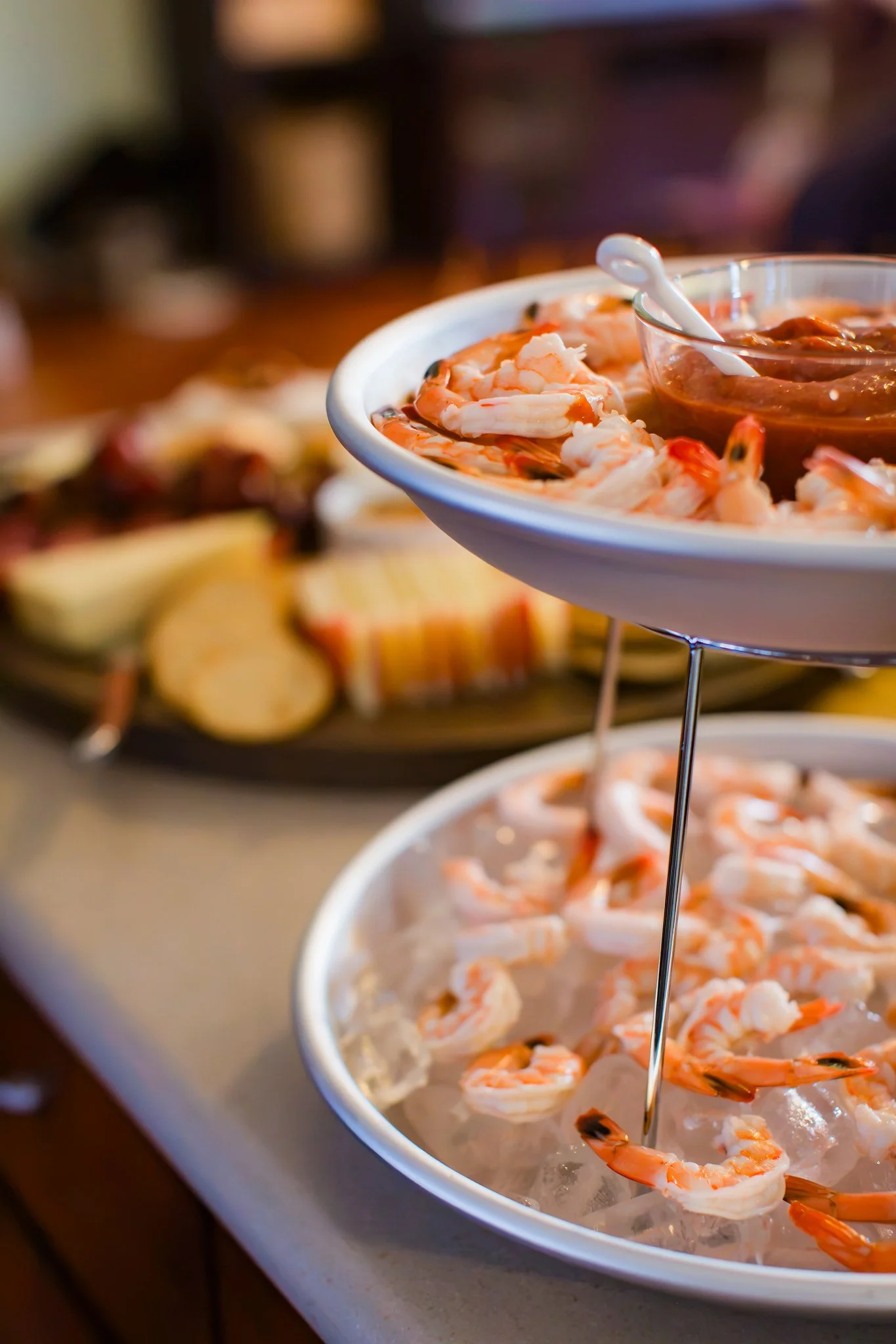 A tiered serving tray with shrimp on ice and a small bowl of cocktail sauce, kitchen or restaurant setting.