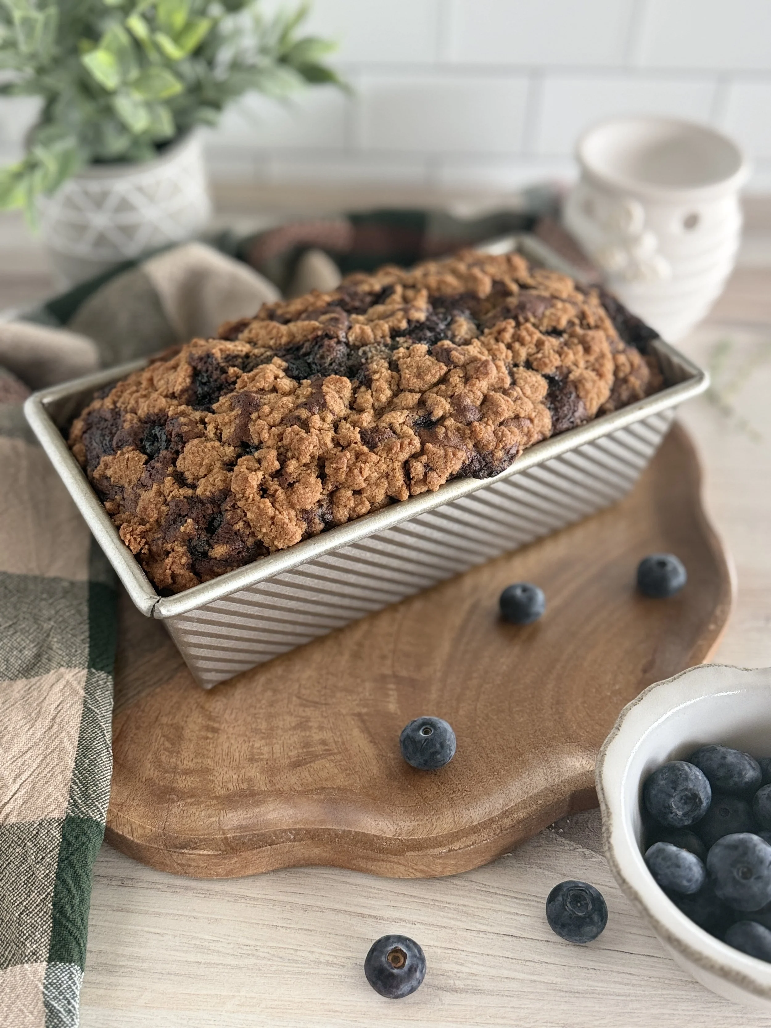 Blueberry bread with crumble on top in a pan on a brown wooden board.