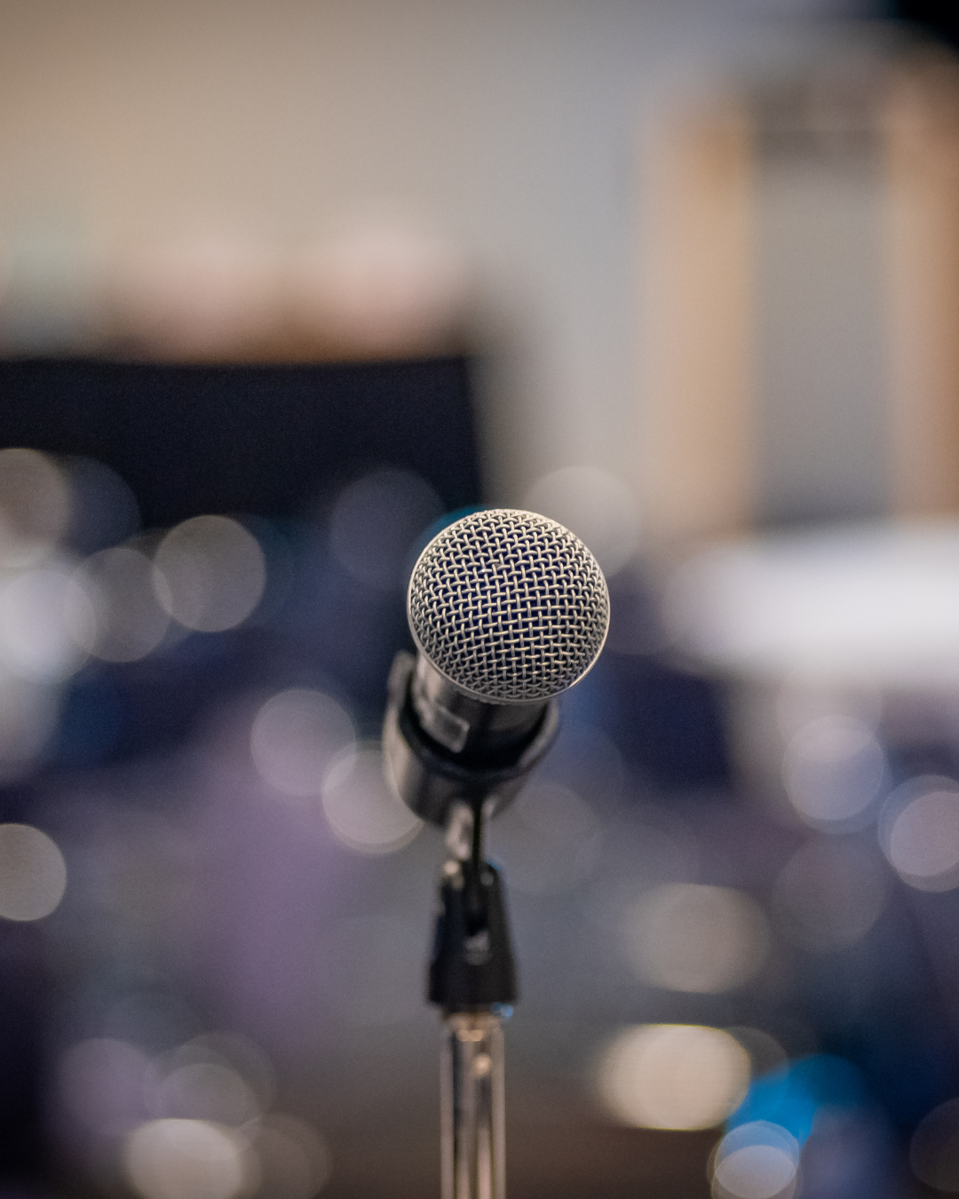 A professional microphone on a stand in a recording studio, blurred background with circular light reflections.