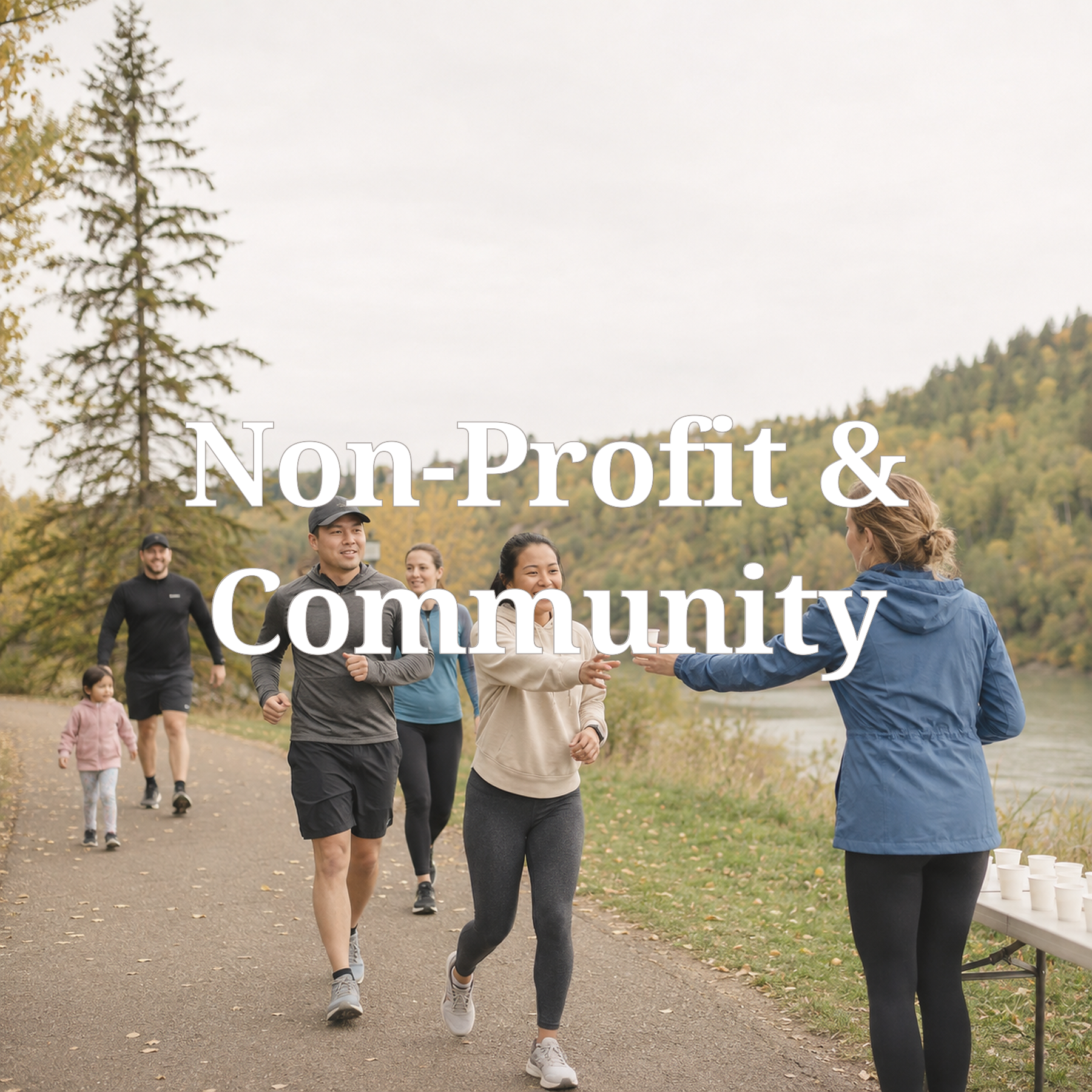 Group of people walking along a trail near a body of water in a park with autumn trees and hills in the background, participating in a community event.