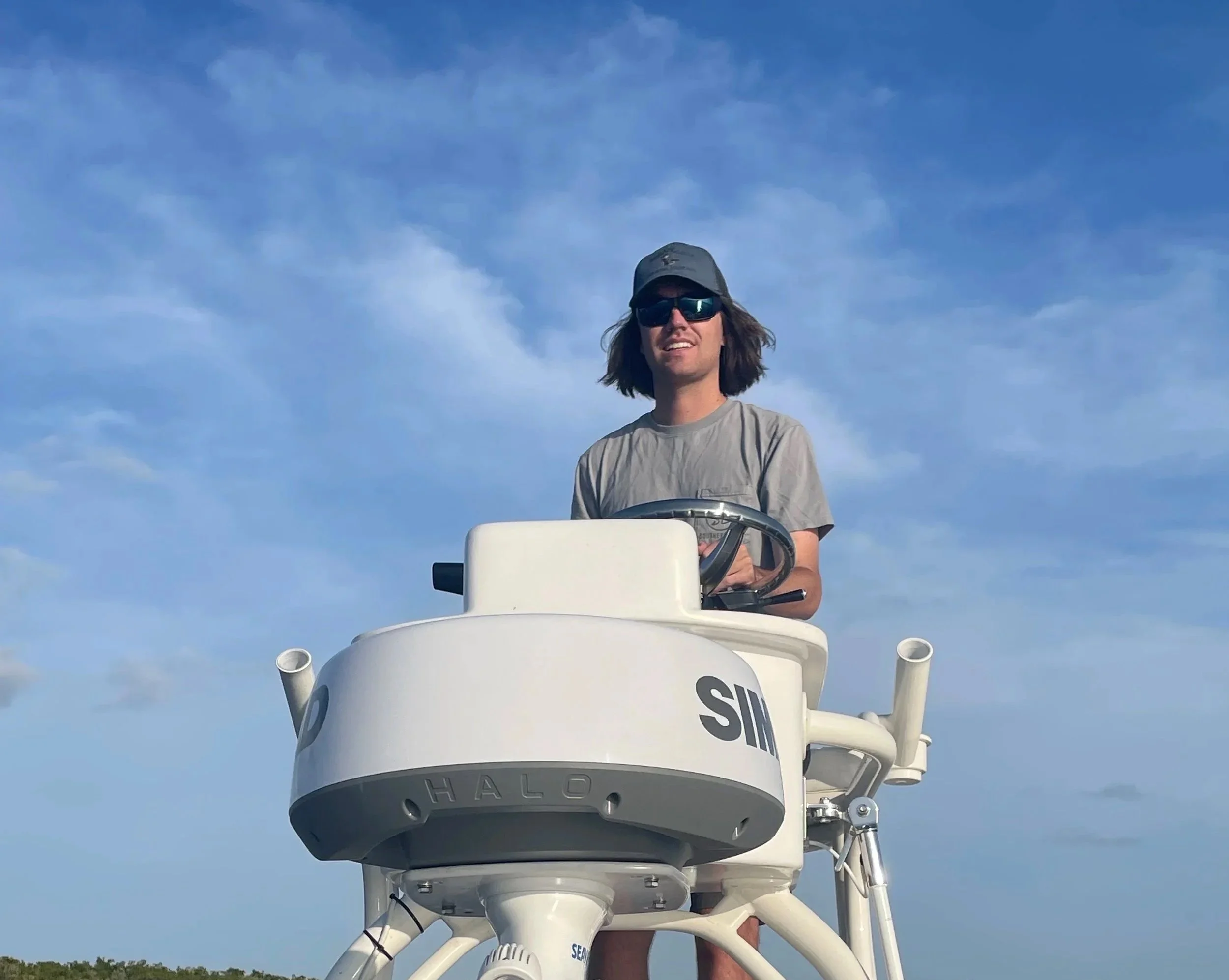 Man operating a satellite dish or radio telescope against a blue sky with scattered clouds.