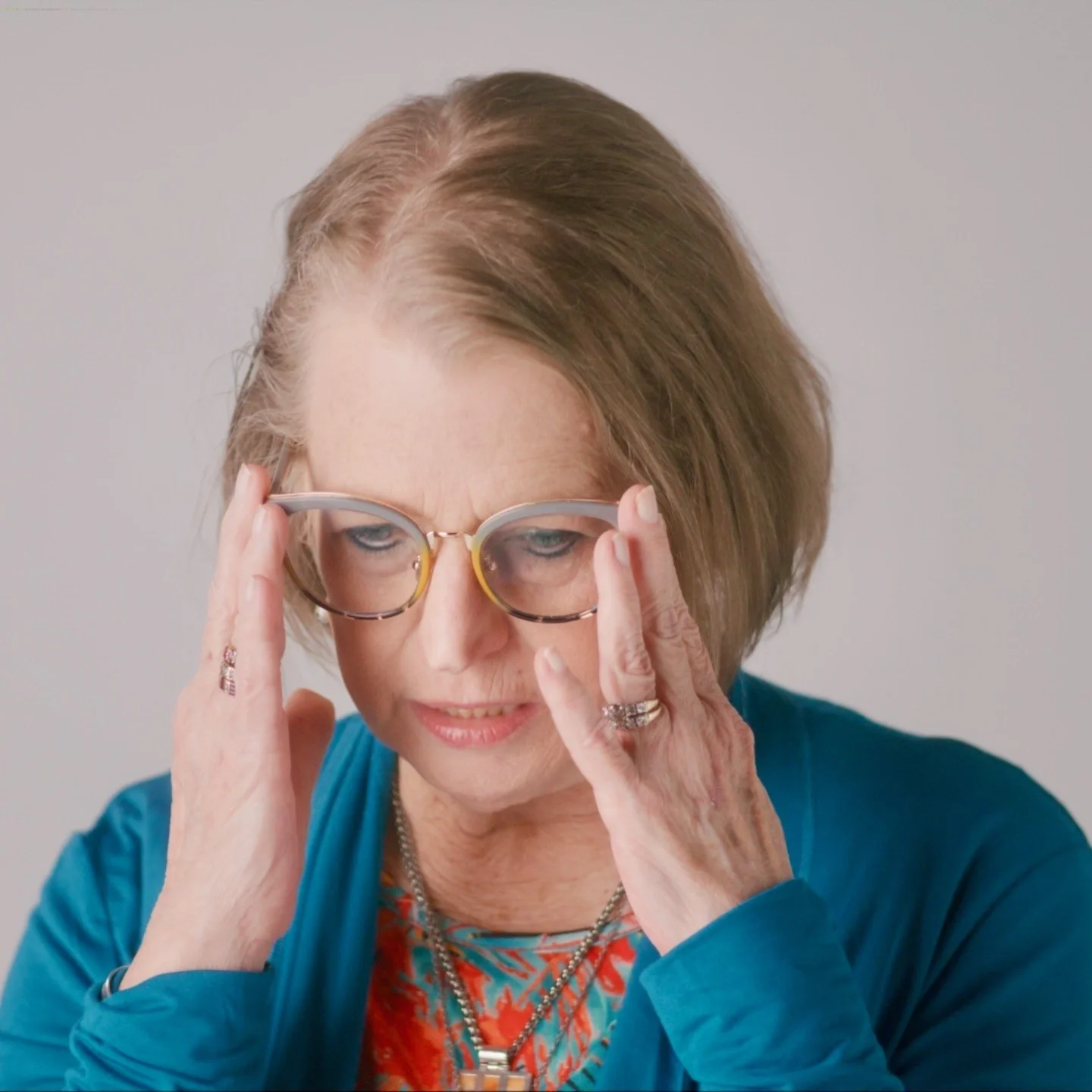 A woman with light dark blonde hair adjusting her glasses.